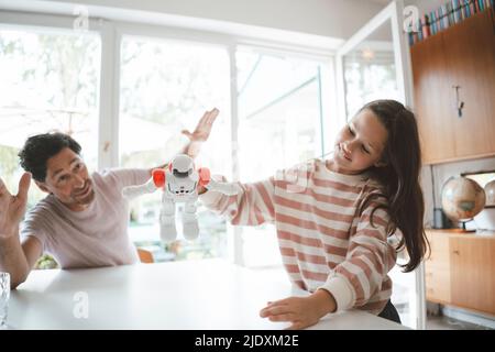 Girl playing with toy robot by father sitting at table Stock Photo