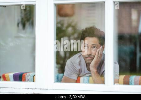 Thoughtful man looking through window Stock Photo