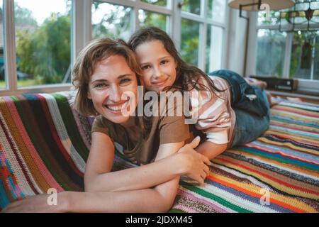 Happy daughter with mother lying on sofa at home Stock Photo