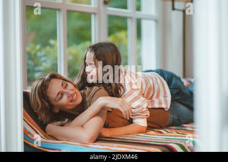 Smiling daughter with mother lying on sofa at home Stock Photo