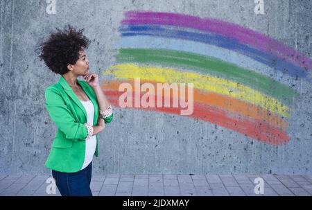 Young woman looking at painted rainbow flag on wall Stock Photo