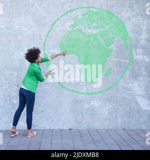 Woman looking at wall with painted globe Stock Photo