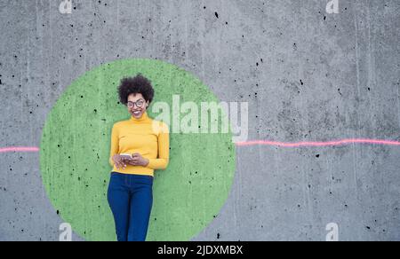Woman using smartphone leaning on wall with green circle Stock Photo