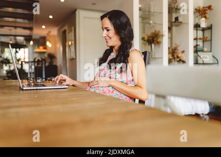 Smiling pregnant woman using laptop sitting at table Stock Photo