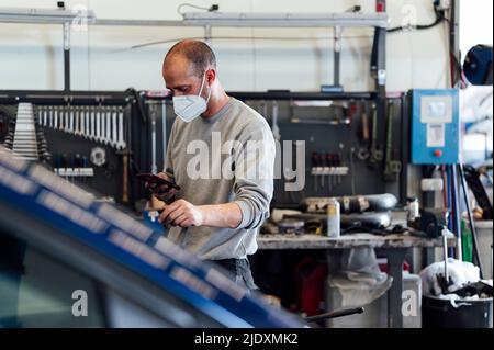 Mechanic using mobile phone in auto workshop Stock Photo