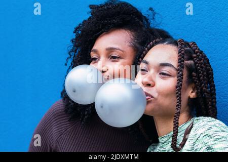 Friends blowing gum bubbles in front of blue wall Stock Photo