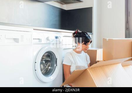 Woman looking in cardboard box sitting by washing machine in utility room Stock Photo