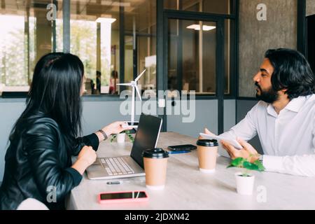 Multiracial colleagues discussing over wind turbine at desk in office Stock Photo