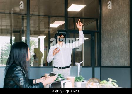 Businessman gesturing with VR glasses by colleague in office Stock Photo