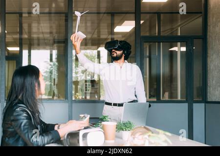 Businessman with VR glasses holding wind turbine model by colleague at work place Stock Photo