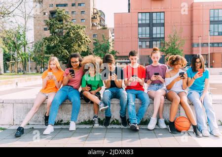 Friends using smart phones sitting on wall Stock Photo