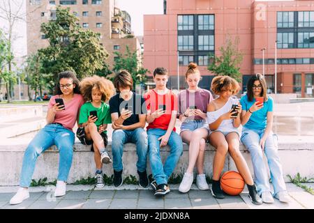 Group of friends using smart phones sitting on wall Stock Photo