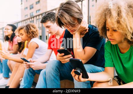 Friends using mobile phone sitting by railing Stock Photo