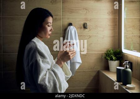 Woman with long hair standing in bathroom wearing bathrobe Stock Photo