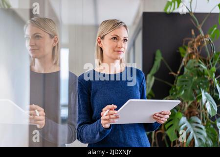Businesswoman with digital tablet in office thinking Stock Photo