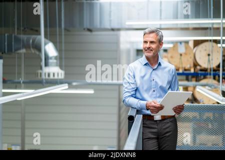 Smiling mature businessman holding digital tablet in factory Stock Photo
