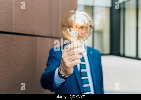 Senior businessman holding light bulb standing by wall Stock Photo