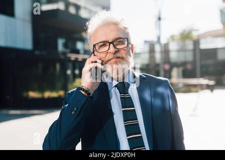 Senior businessman wearing eyeglasses talking on smart phone outdoors Stock Photo