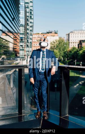 Senior businessman wearing virtual reality simulator standing by railing on sunny day Stock Photo