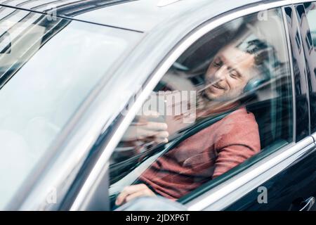 Smiling man using smart phone sitting in car Stock Photo