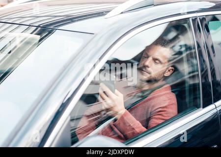 Man using smart phone sitting in car seen through window Stock Photo