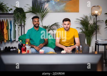 Young men watching football match sitting on sofa at home Stock Photo