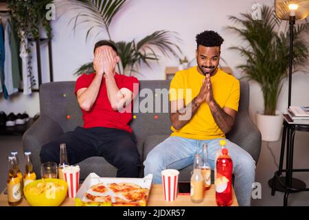 Young man sitting with hands covering face by roommate on sofa at home Stock Photo