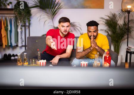 Surprised young man talking with curious friend watching football match at home Stock Photo