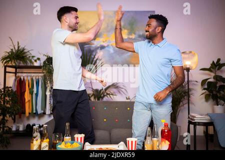 Happy young men giving high-five to each other standing in living room at home Stock Photo