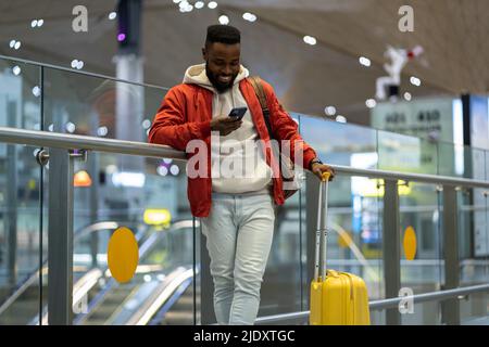 Smiling African American guy using smartphone, checking incoming messages after arrival to airport Stock Photo