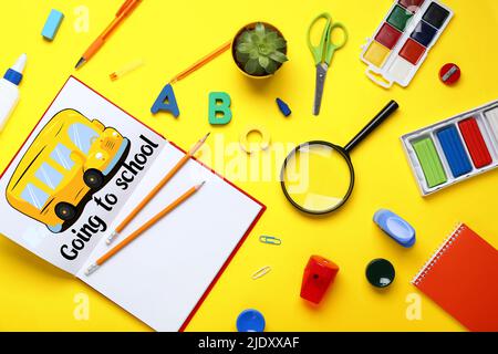 Set of stationery, notebook with drawn bus and text GOING TO SCHOOL on yellow background Stock Photo