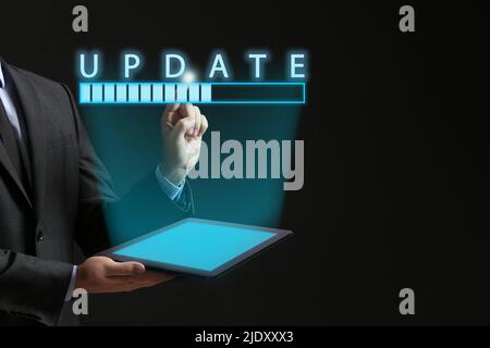 Businessman with tablet computer using virtual screen with word UPDATE and status bar on dark background Stock Photo