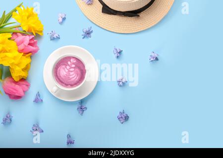 Cup of pink matcha tea with beautiful spring flowers and hat on blue background Stock Photo