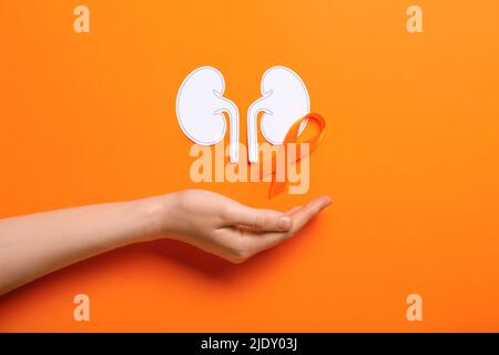 Woman with awareness ribbon and paper kidneys on orange background Stock Photo