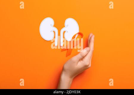 Woman with awareness ribbon and paper kidneys on orange background Stock Photo