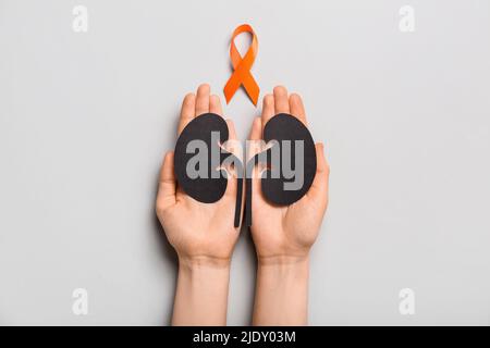 Woman with orange awareness ribbon and paper kidneys on grey background Stock Photo