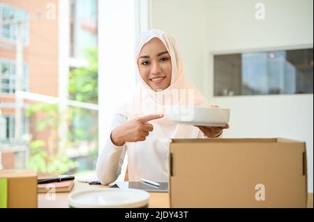 Portrait of a beautiful successful young muslim female online business entrepreneur showing her cookware product to camera. E-commerce business concep Stock Photo