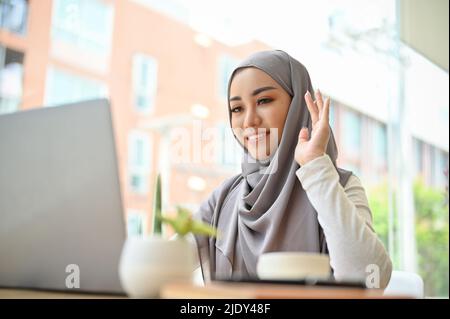 Beautiful asian muslim businesswoman or female college student wearing hijab having an online meeting conference with her coworker. Stock Photo
