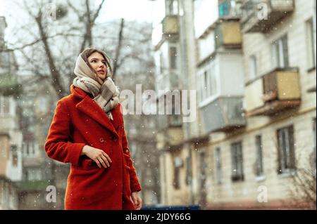Beautiful brunette in a red coat on a city street under the snow. Stock Photo