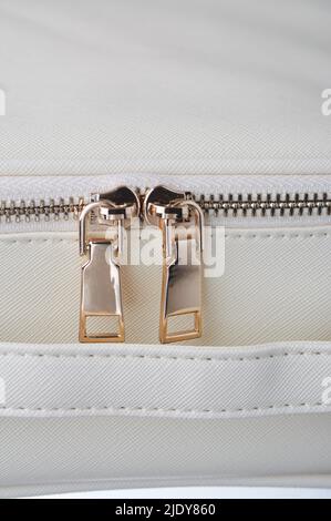gold zippers with gold zippers are fastened on a white leather object, close-up Stock Photo