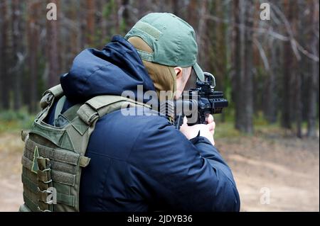 a man in camouflage shoots from a machine gun in the forest Stock Photo