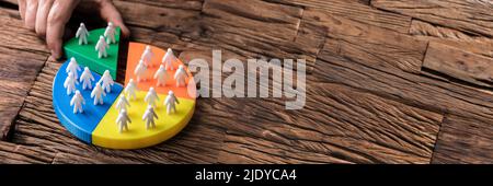 Human Hand Placing A Last Piece With Human Figures Into Pie Chart On Wooden Desk Stock Photo