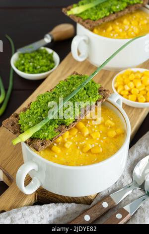 Corn soup with fresh garlic pate in white bowl. Healthy food on black wooden background. Vegan cuisine. Traditional autumn corn soup. Served with corn Stock Photo
