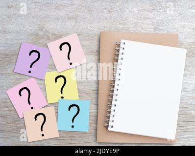 Question mark on pink sticky notes and blank notebook on wood table background. Business and education concept design. Stock Photo