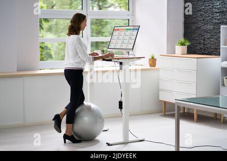 Woman Using Adjustable Height Standing Desk In Office For Good Posture Stock Photo