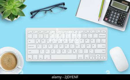 Office desk with stationary,keyboard,notebook,calculator,pencil,coffee and flower on blue table background. Top view with copyspace. Concept for busin Stock Photo