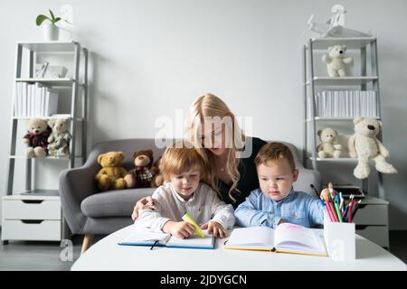 Teacher mom working with creative kids. Teacher helps school kids to learn lesson. Stock Photo