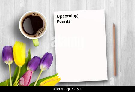 Text with Upcoming Events and coffee cup, notebook,pencil on white wooden table. Top view with copy space (selective focus). Office desk table,food an Stock Photo