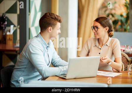 Content young team of marketing specialists sitting at table with laptop and working on project together Stock Photo