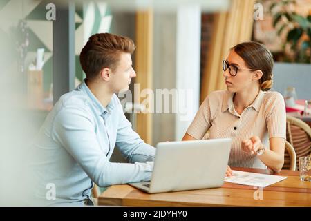 Busy young business colleagues in casual clothing sitting at table and analyzing sales while working on new project Stock Photo